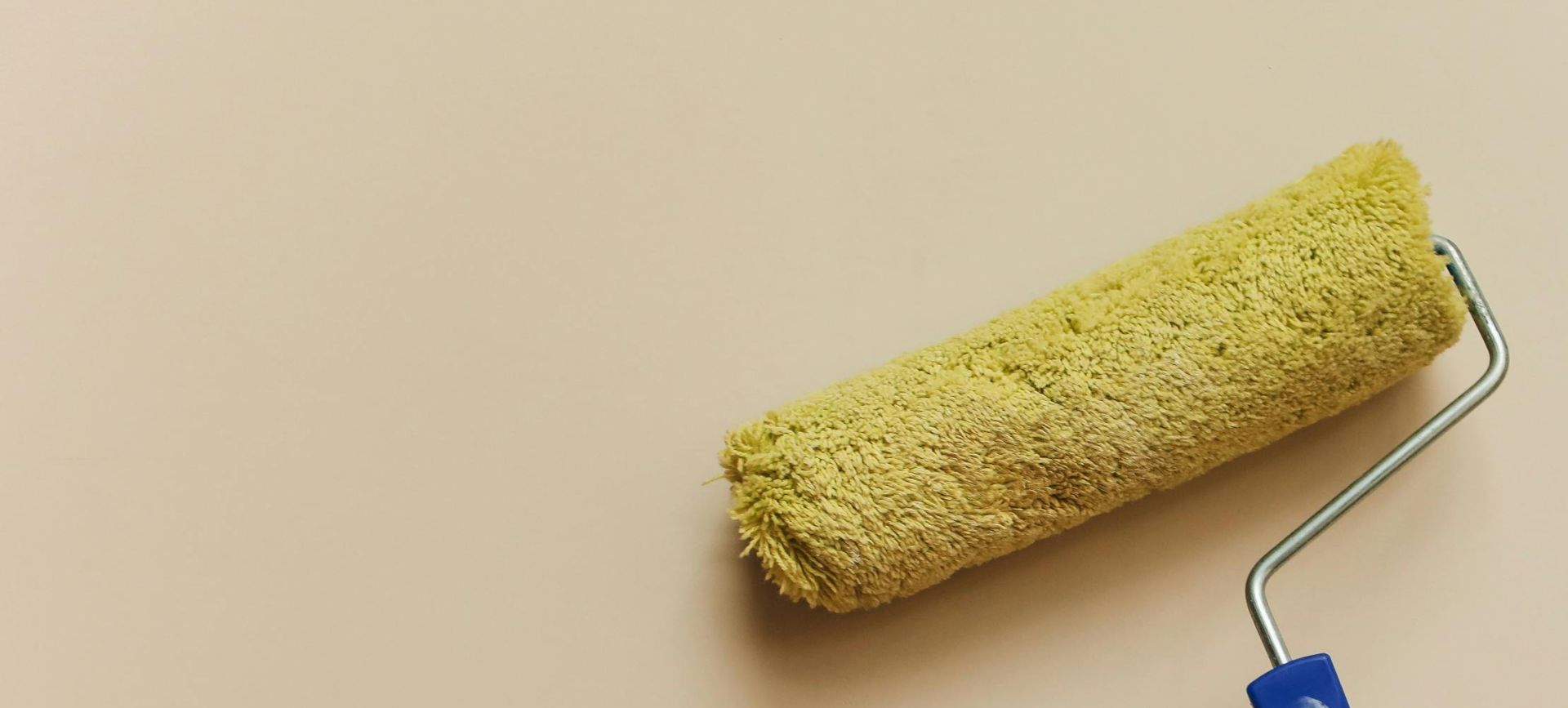 A hand using a yellow paint roller to paint a beige wall. Perfect for DIY and home improvement themes.